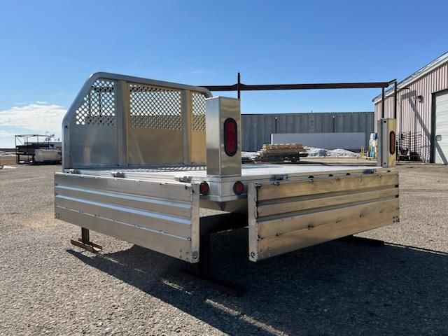 A large aluminum trailer is parked in a gravel lot in front of a building.