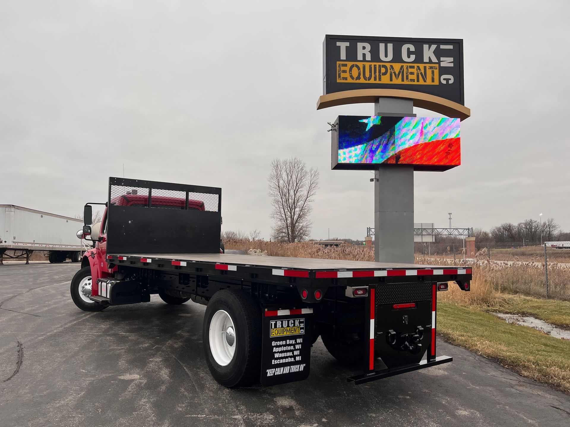 A flatbed truck is parked in front of a truck equipment sign.