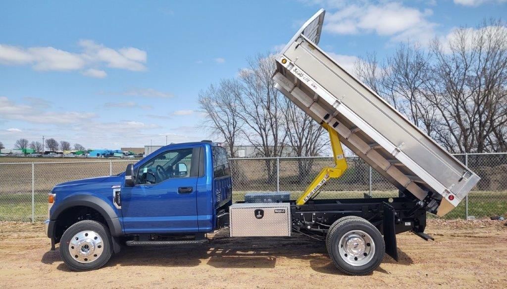 A blue dump truck is parked in a dirt field.