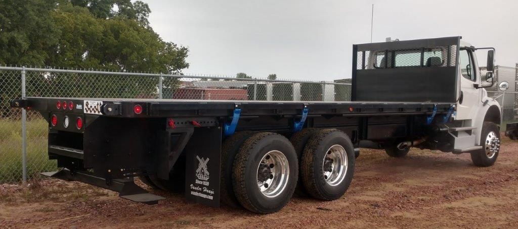 A flatbed truck is parked in a dirt field next to a chain link fence.