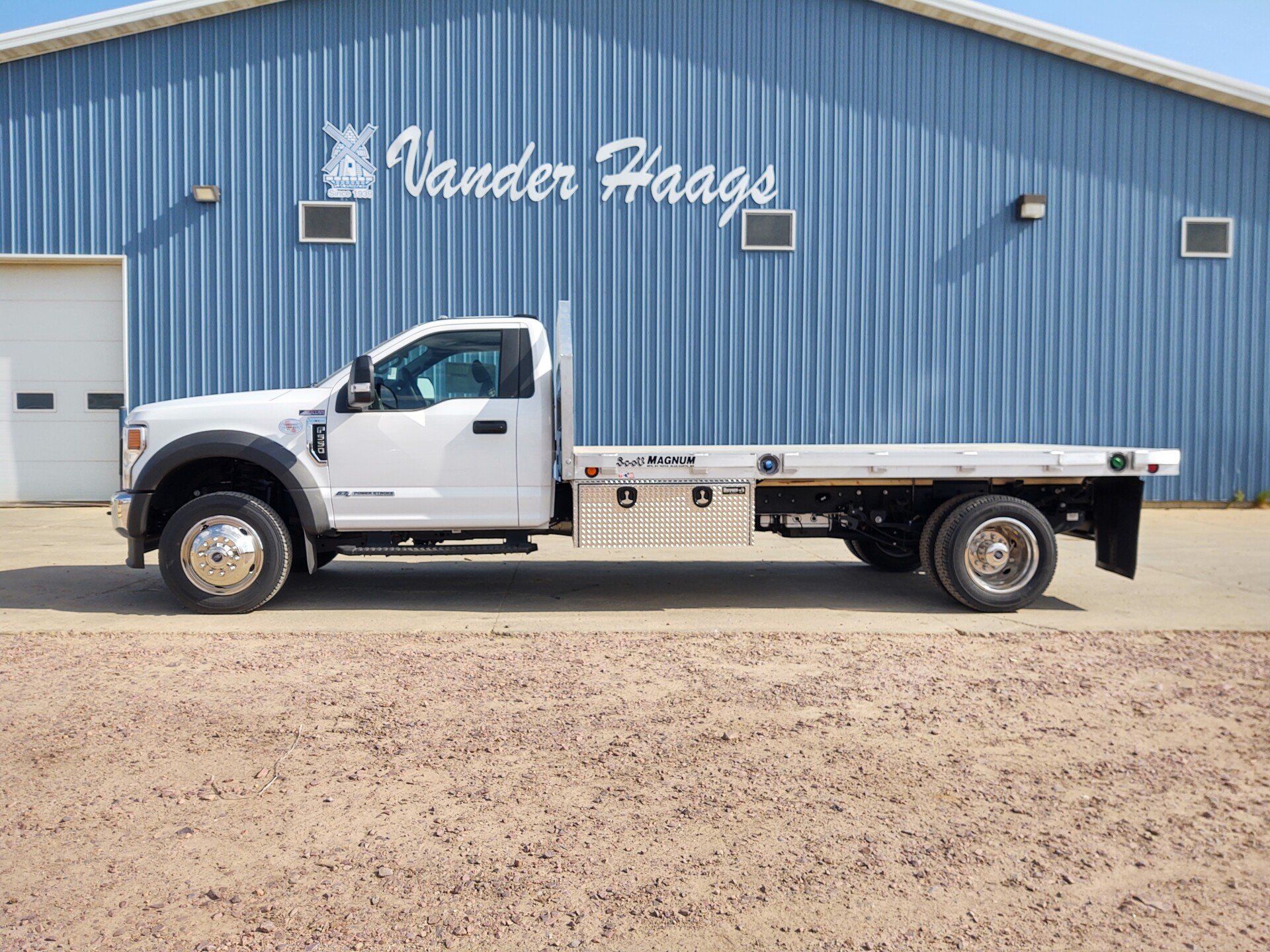 A white flatbed truck is parked in front of a blue building.