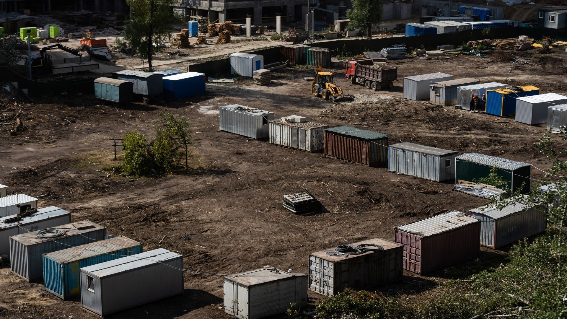 Rows of shipping containers on a dirt lot, with construction materials scattered around a work site.