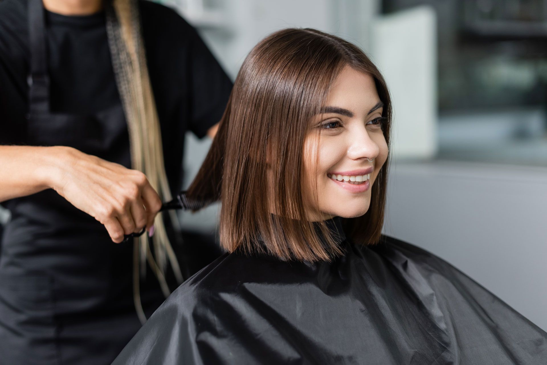 Woman getting her hair cut at a salon, smiling. Hairdresser in black cutting hair.