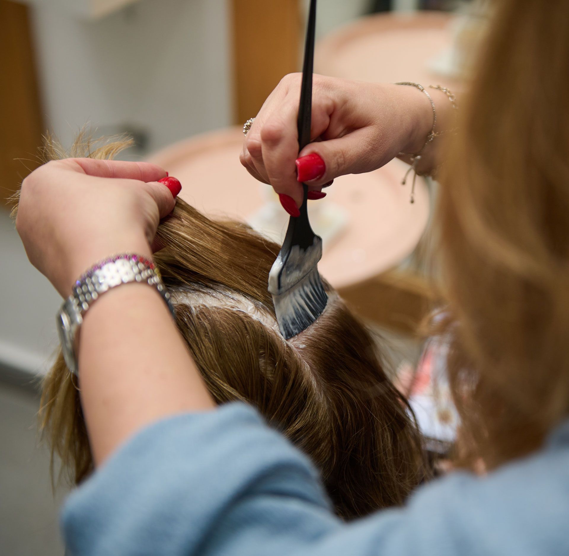 Hands applying hair dye with a brush to light brown hair.