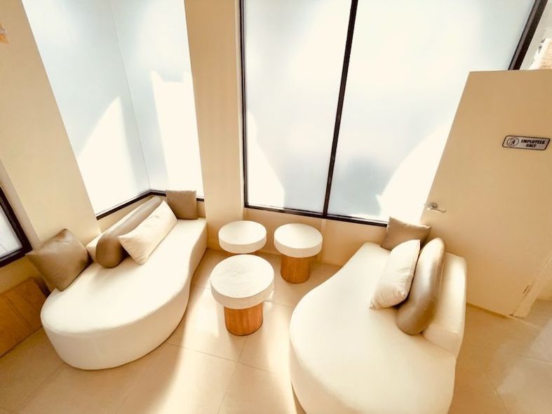 Bright lounge area with curved cream sofas, small white tables, and large windows.