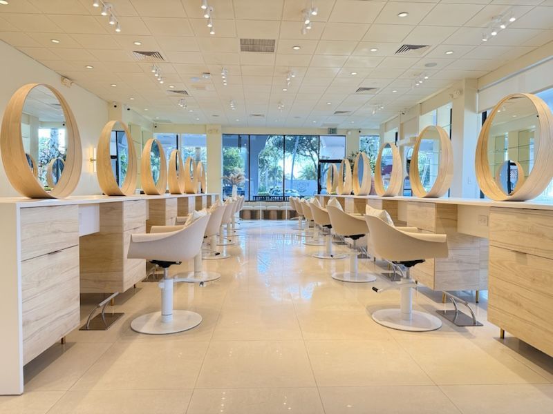 Hair salon interior with light-colored styling stations, round mirrors, and chairs.