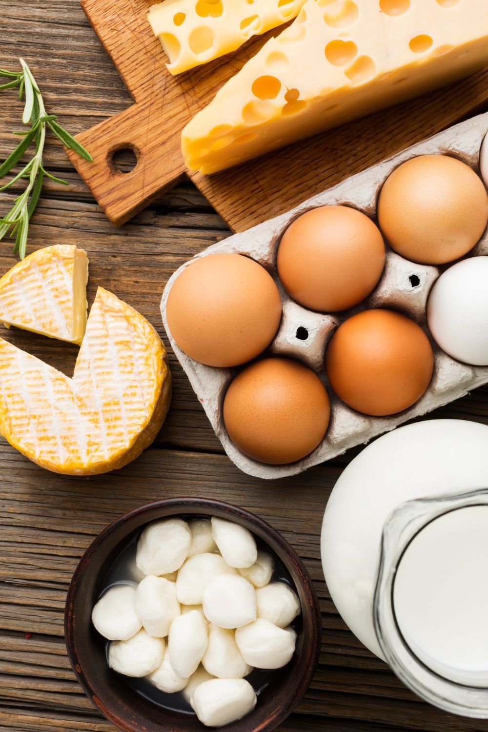 Una variedad de productos lácteos, incluyendo queso, leche y huevos, dispuestos sobre una superficie rústica de madera.