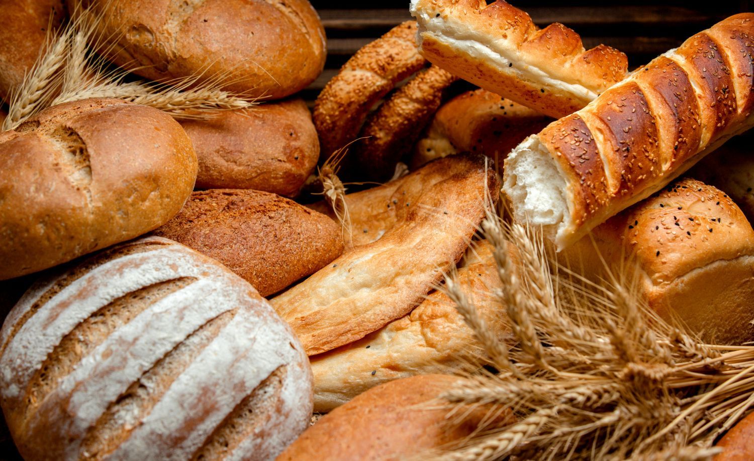 Una variedad de panes artesanales, que incluyen hogazas, panecillos y una baguette, dispuestos con espigas de trigo.