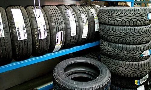 Montones de neumáticos negros para coches sobre estanterías azules en una tienda de neumáticos.