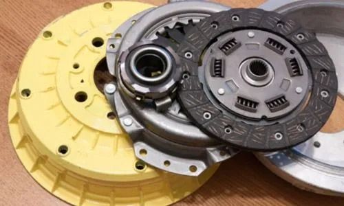 Componentes de embrague automotriz de color amarillo y gris dispuestos sobre una superficie de madera.