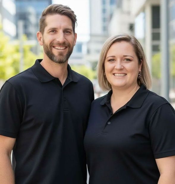 Two people in black polos standing outdoors in front of modern buildings, smiling at the camera