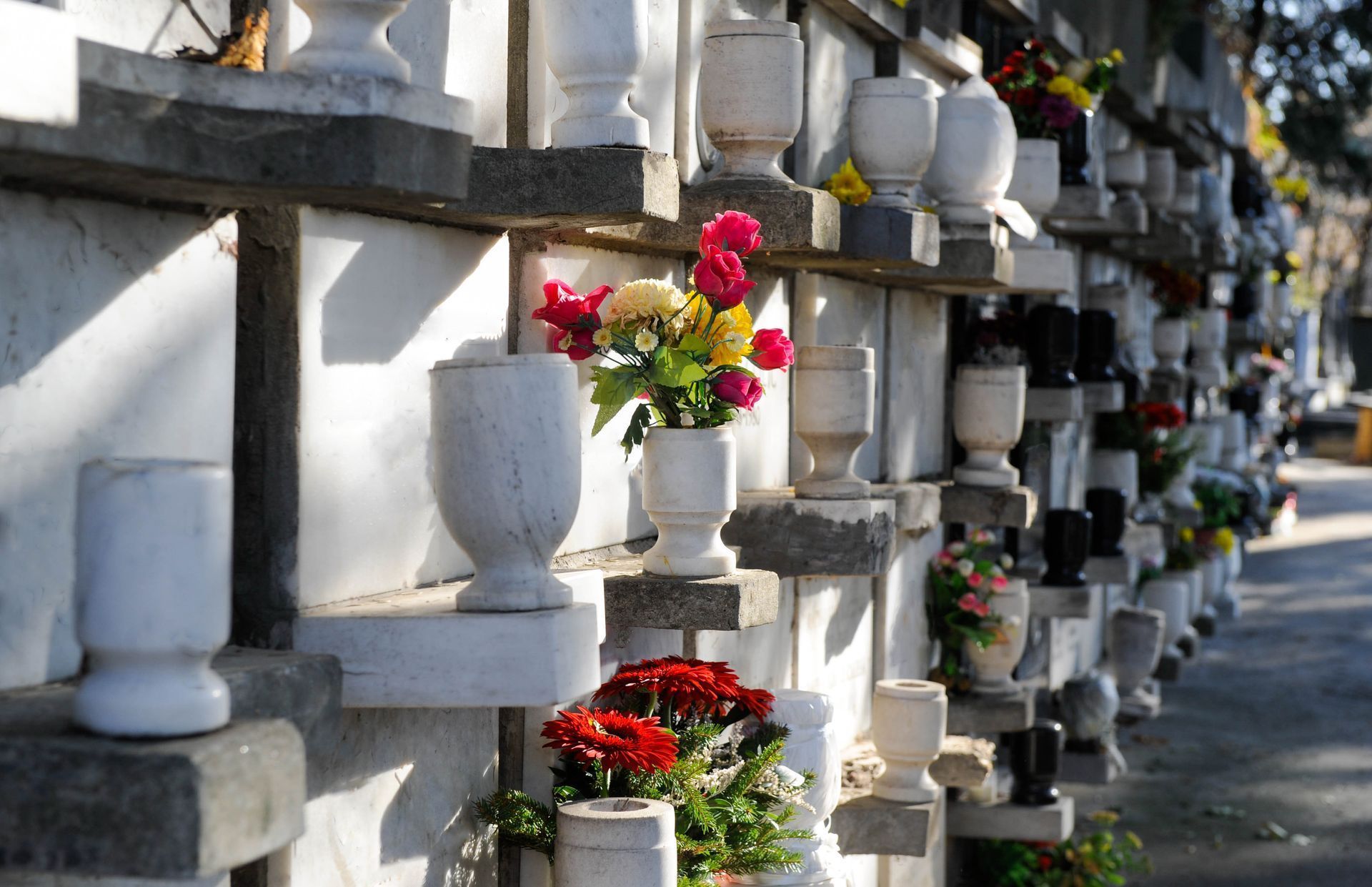 Rows of white marble crypts in a cemetery, with vases of flowers.