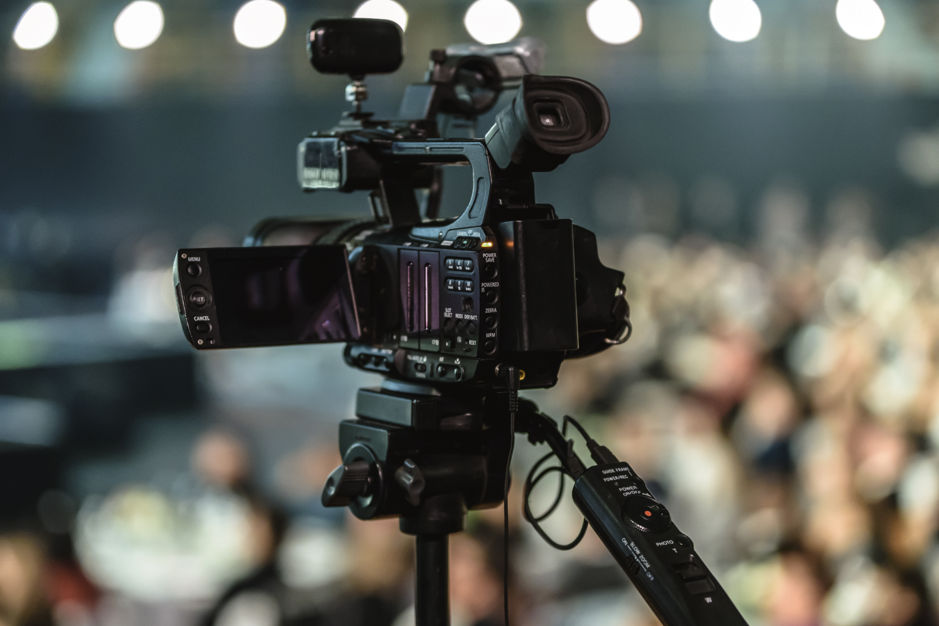 A video camera is sitting on a tripod in front of a crowd of people.