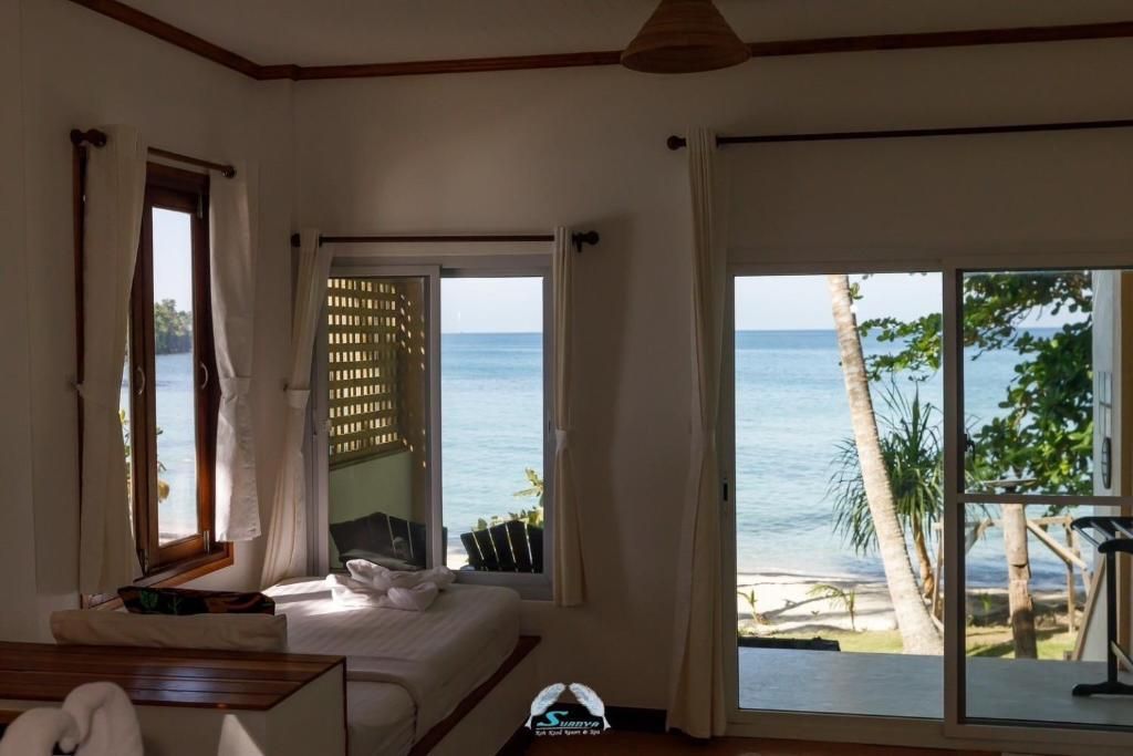 Interior view of a room with a bed, windows, and an ocean view. White walls and curtains.