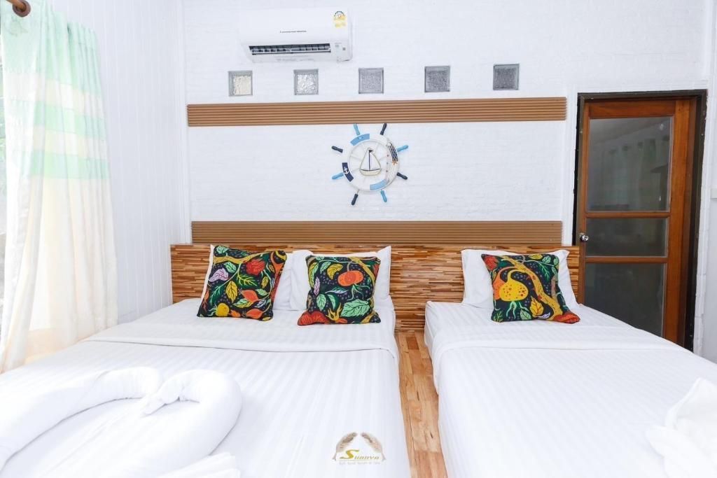 A bright white bedroom with three beds. Decorative pillows on beds, art on wall, and door to the side.