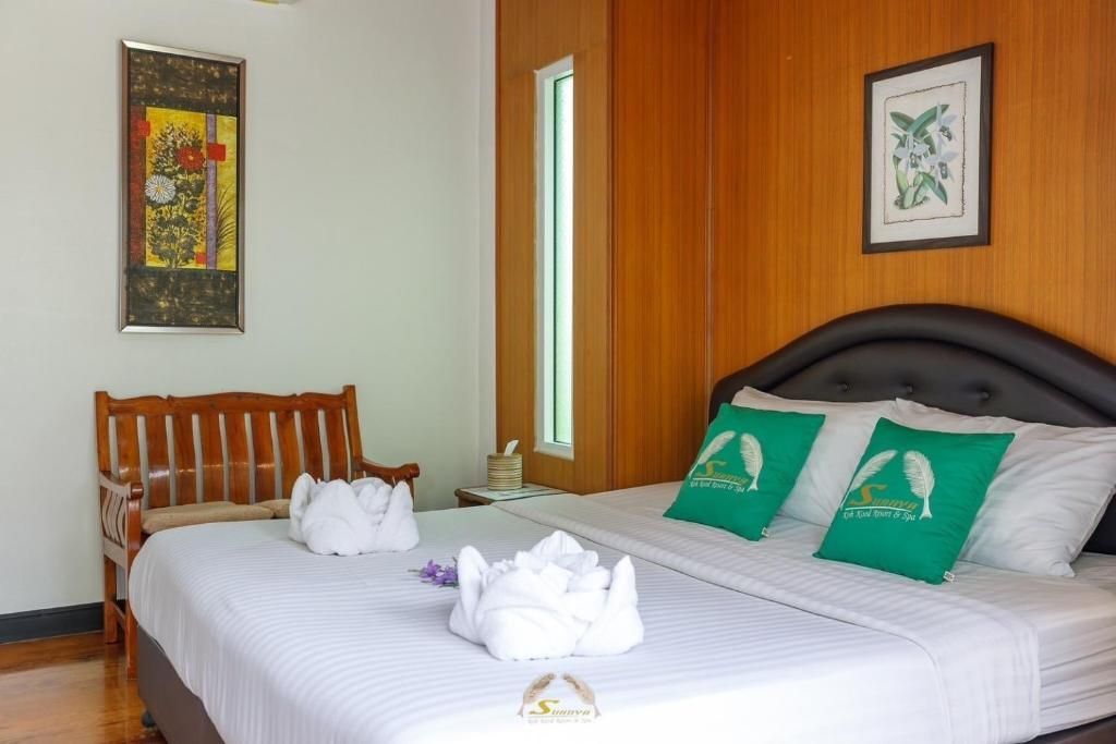 Bedroom with king-sized bed, wood panel walls, decorative pillows, small chair, art, and two towel swans.