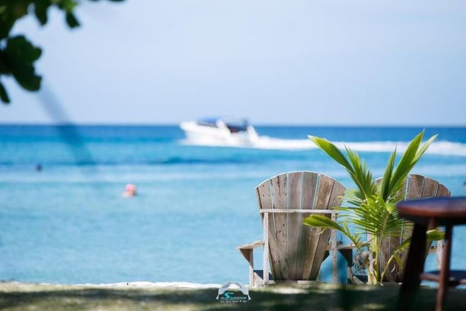Wooden chairs overlooking a turquoise ocean with a boat in the distance.