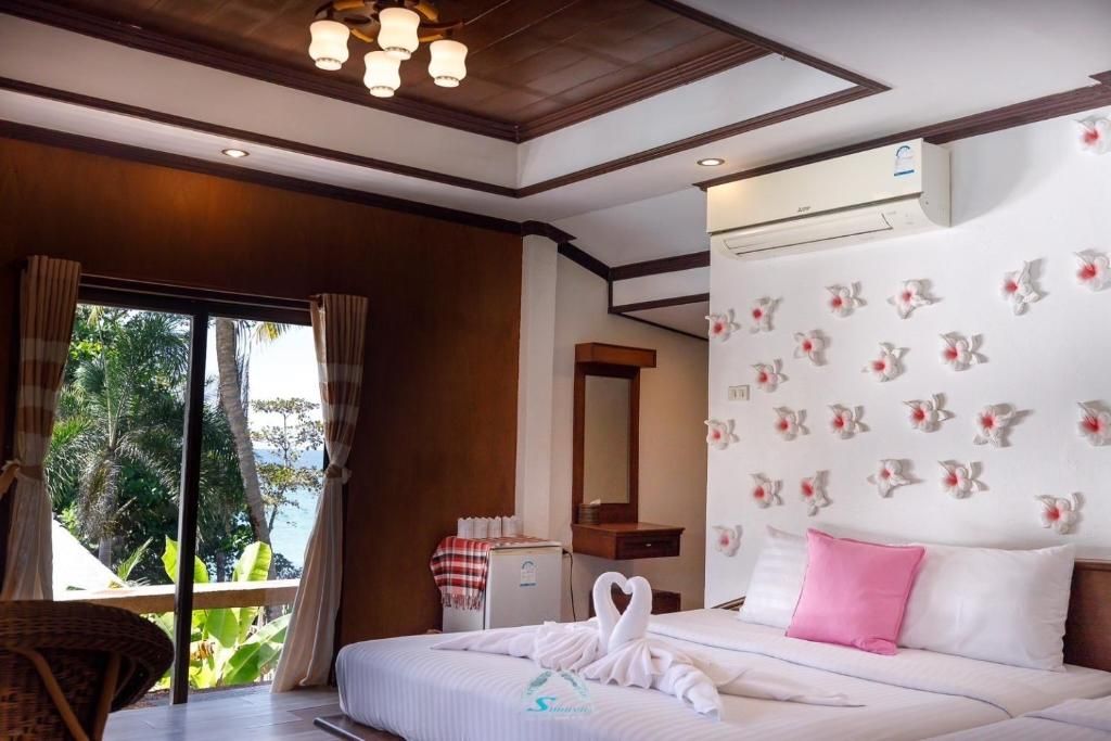 Bedroom with white bed, pink pillow, swan towel, floral wallpaper, and large window.