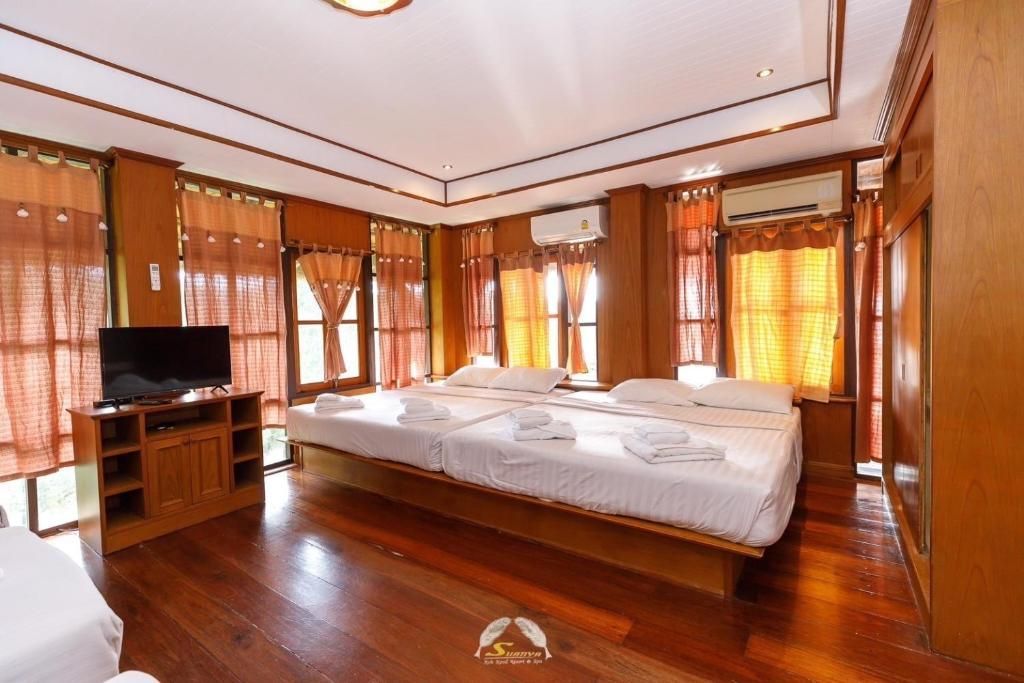 Bedroom with two twin beds, wooden floors and walls, and orange curtains. A TV and air conditioning units are also visible.