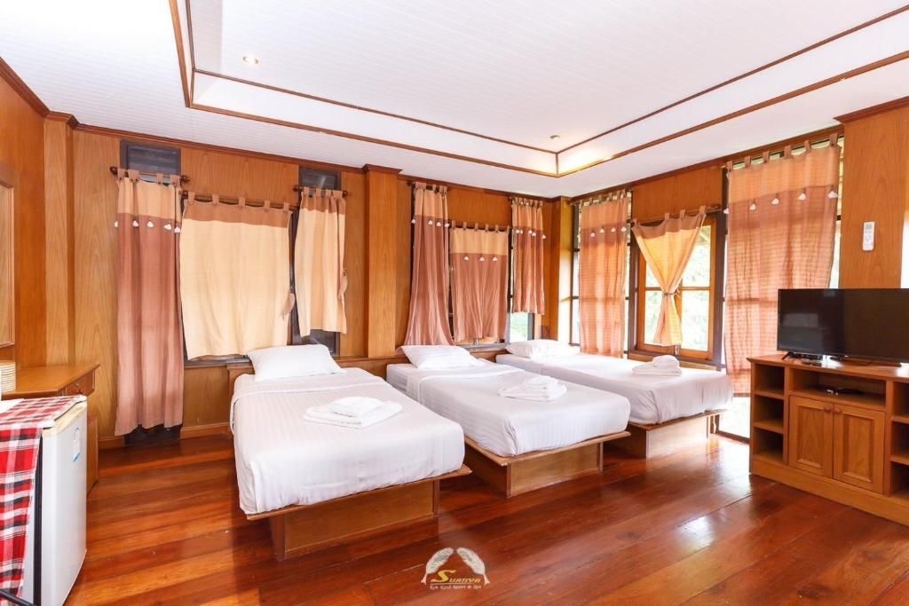 A wooden hotel room with three twin beds, curtains, TV, and a mini-fridge.