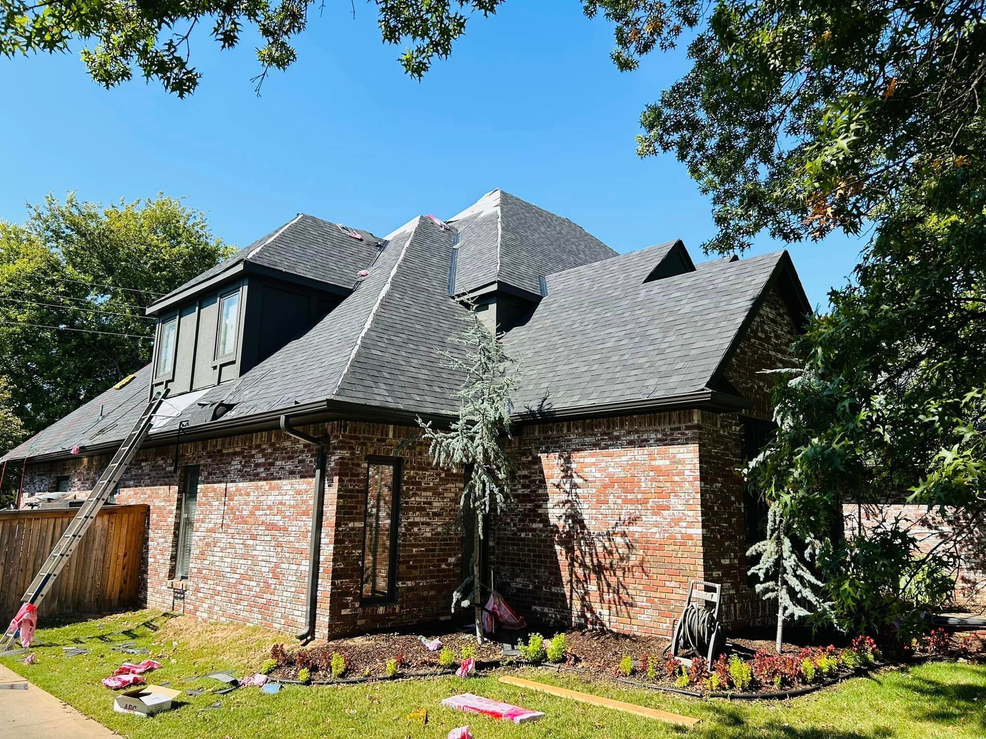 A large brick house with a black roof is being painted.