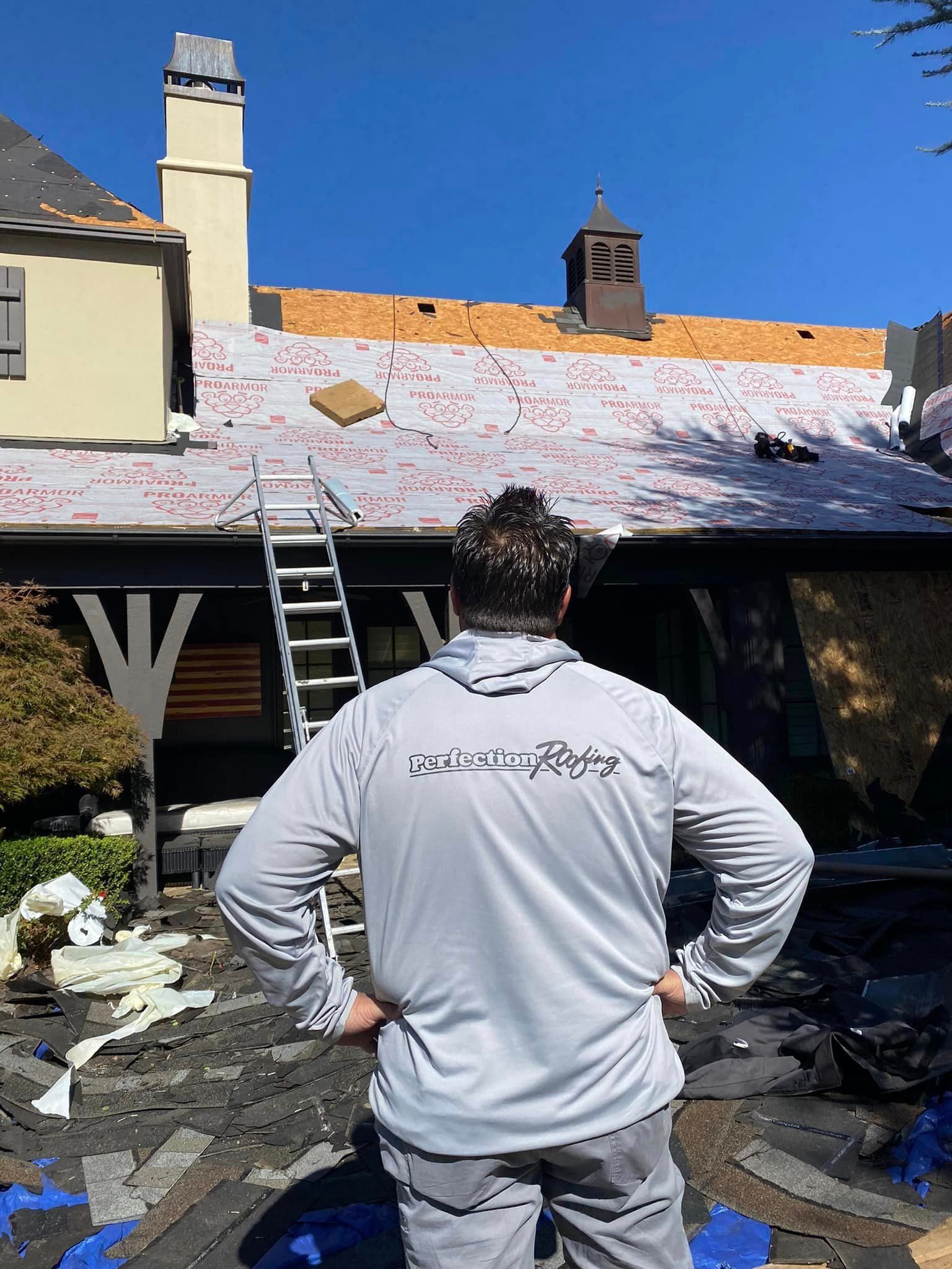 A man is standing in front of a house with a ladder on the roof.