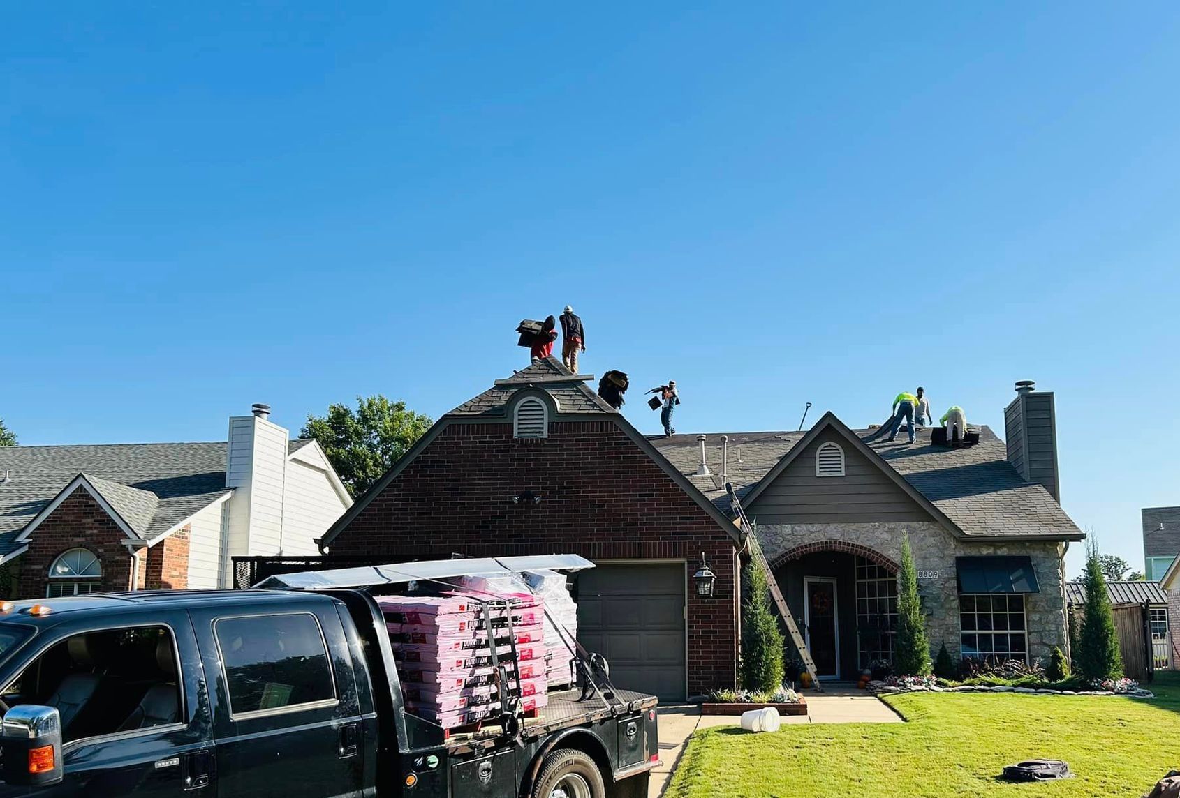 A truck is parked in front of a house with workers on the roof.