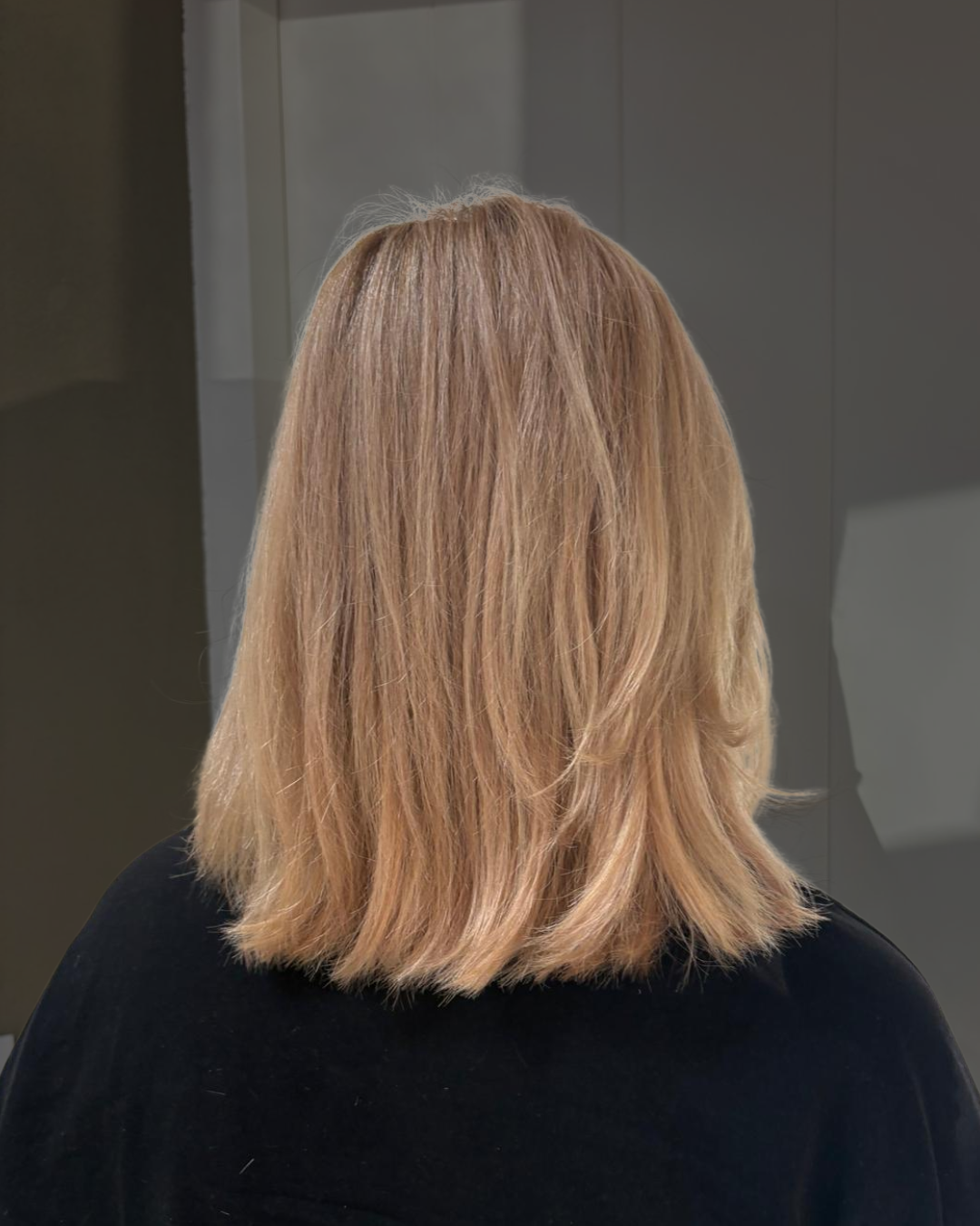 Achteraanzicht van schouderlang blond haar tegen een donkere achtergrond.