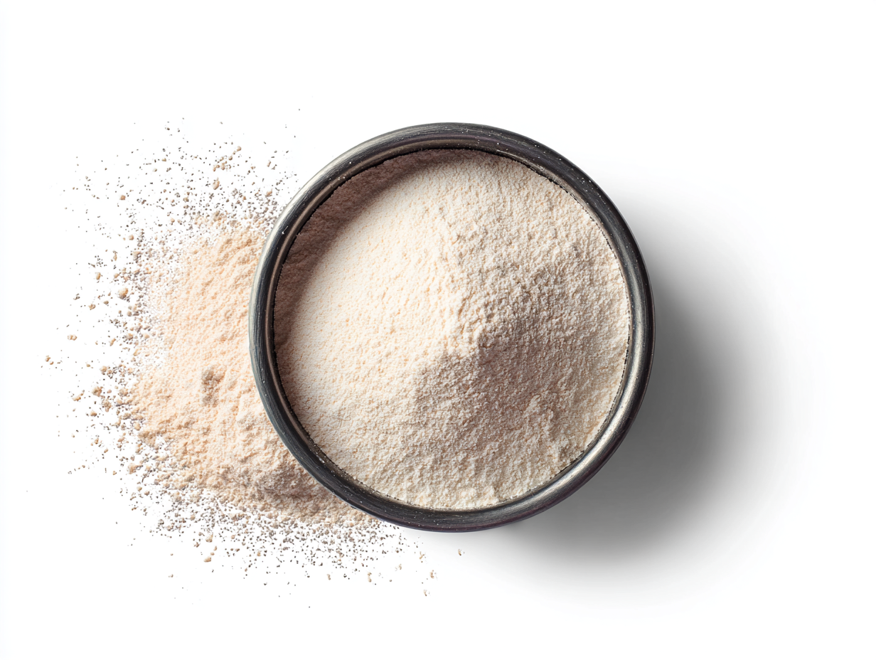 A bowl of light beige powder with some spilled next to it, against a white background.