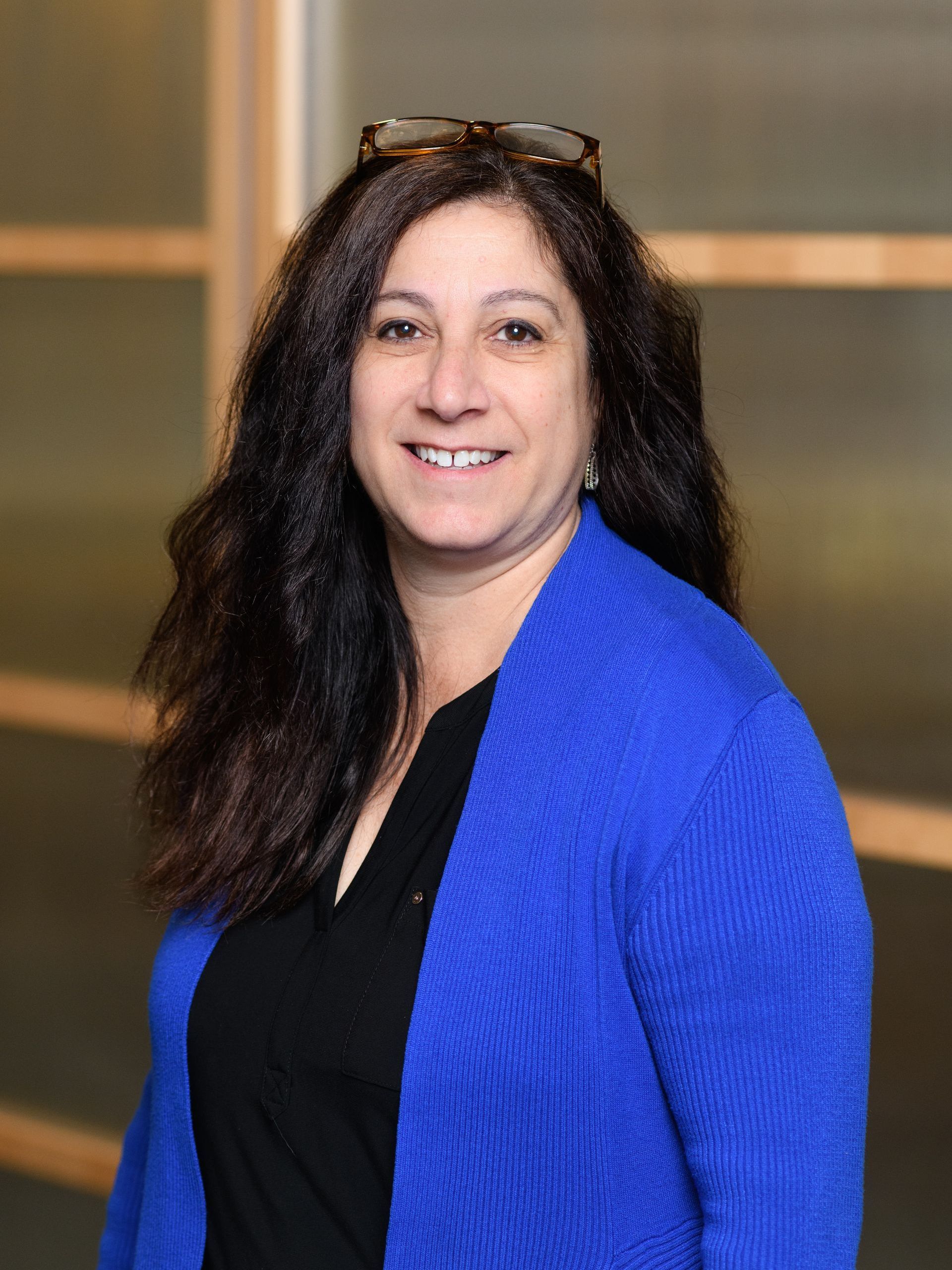 A woman wearing a blue sweater and glasses is smiling for the camera.