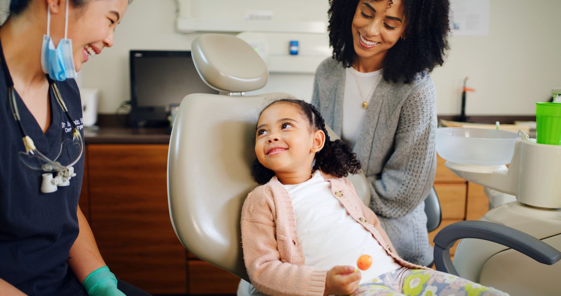 Mother, child with a lollipop, and dentist at a dental office for a checkup.