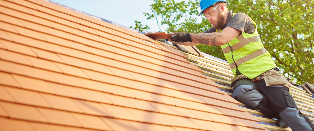 Roofer on a tiled roof in a safety vest and hard hat. He is working on the roof.