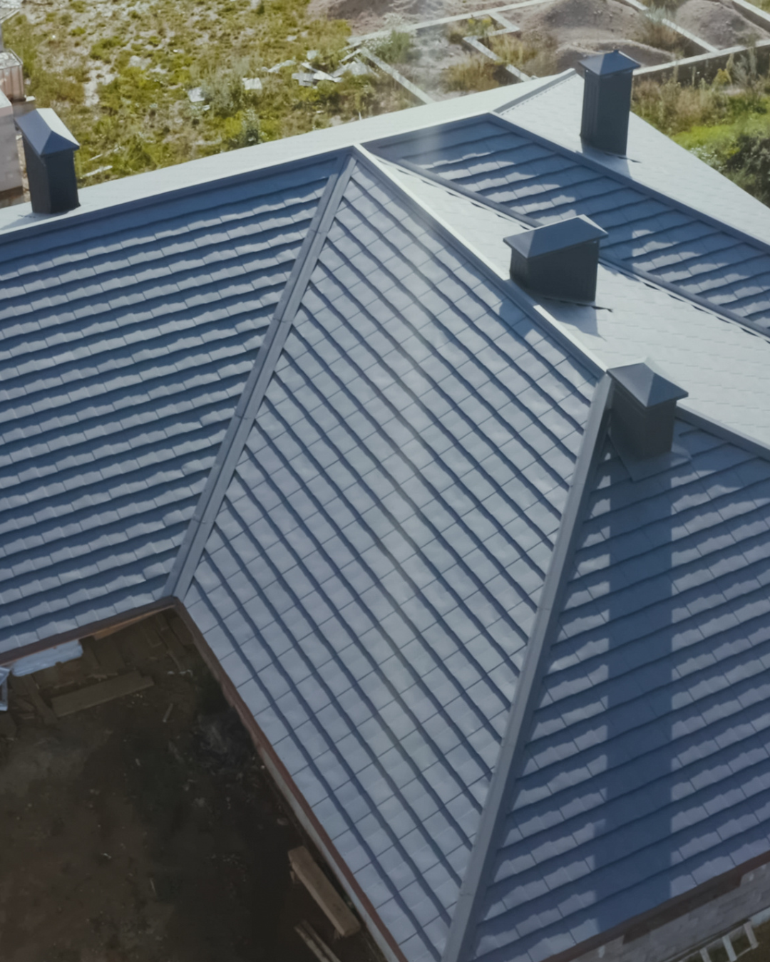 An aerial view of a house with a blue metal roof and chimneys.