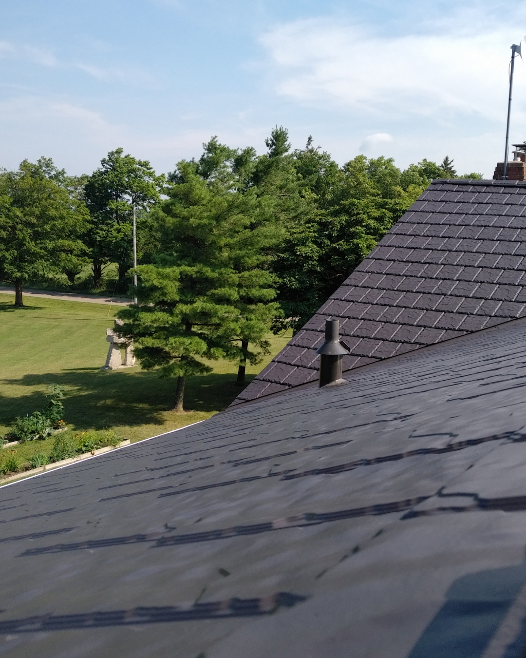 A slate roof with a chimney and trees in the background