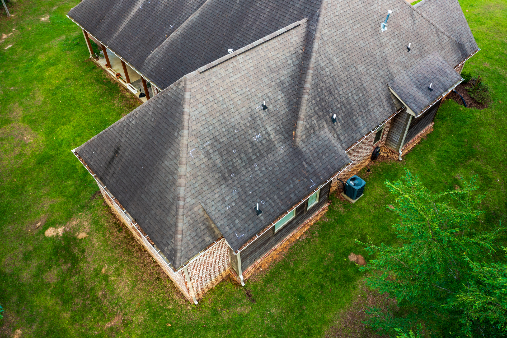Overhead view of a house with a dark roof and brick exterior, surrounded by green grass.