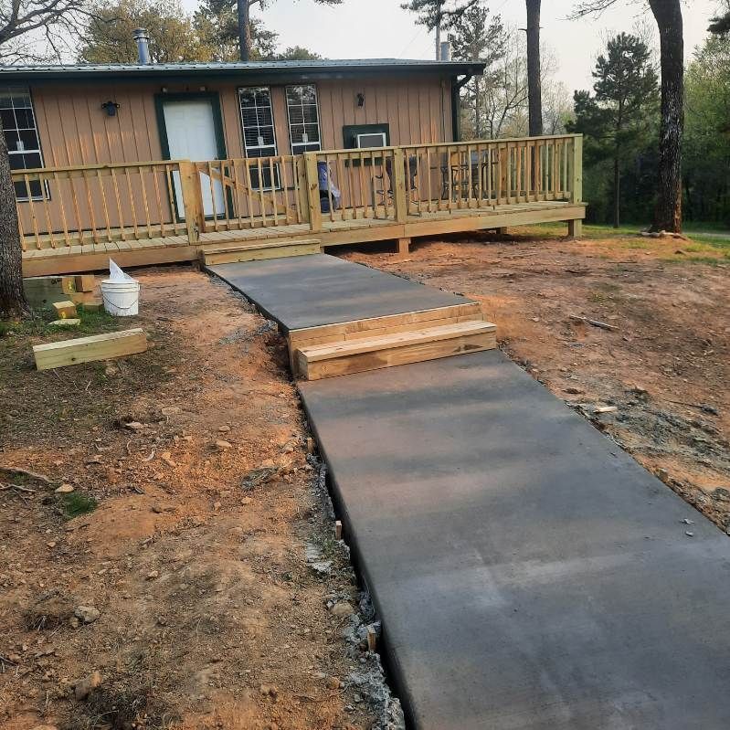 A concrete walkway leading to a house with a deck