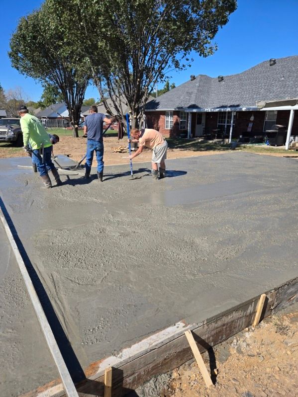 A group of men are working on a concrete driveway in front of a house.