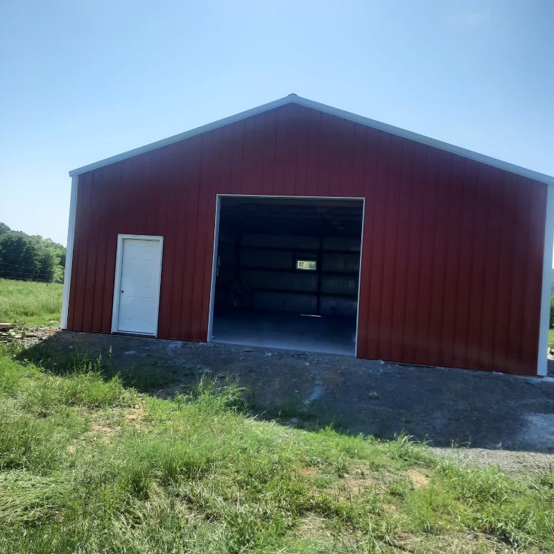 A red barn with a white door is in a grassy field