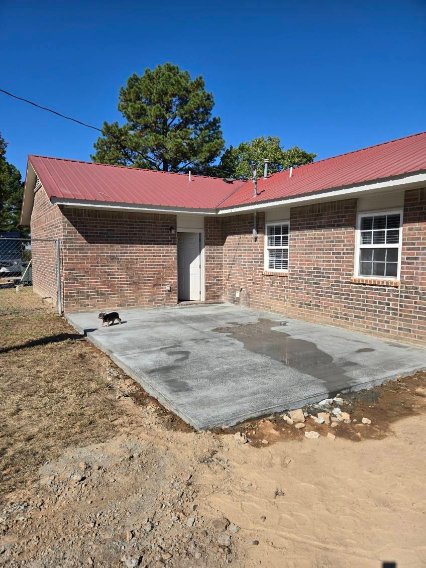 A brick house with a red roof and a concrete patio in front of it.