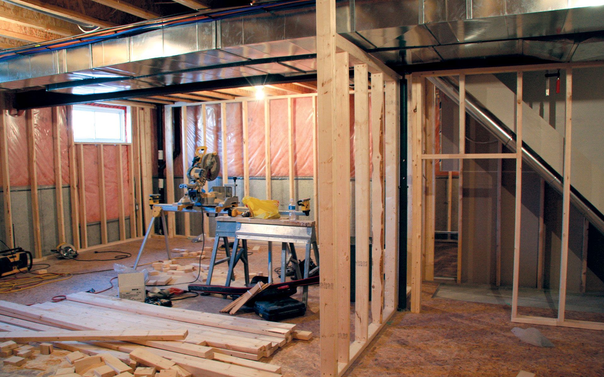 Basement under construction with wood framing, insulation, and tools scattered about.