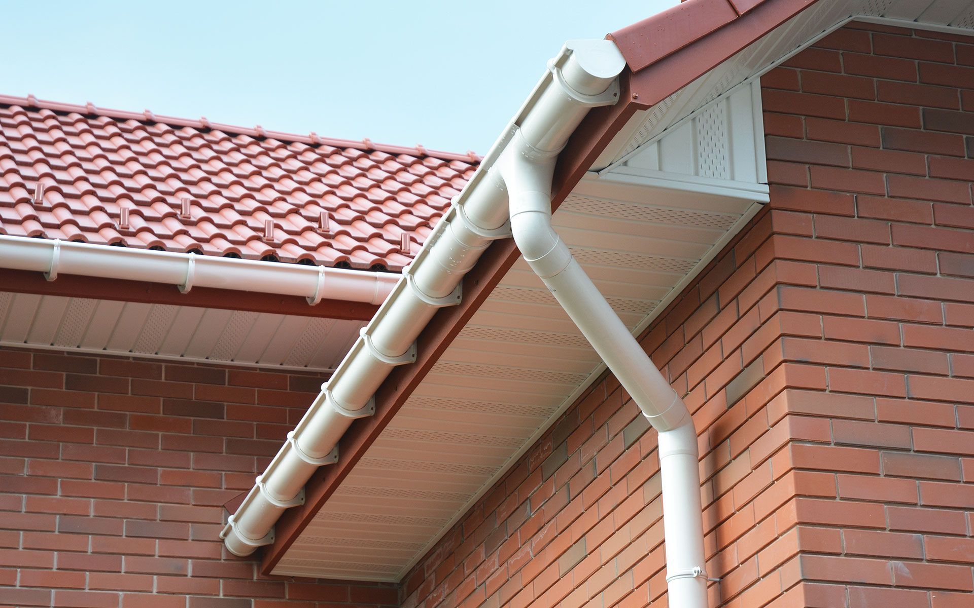 White rain gutters on a red brick building with a red tile roof.