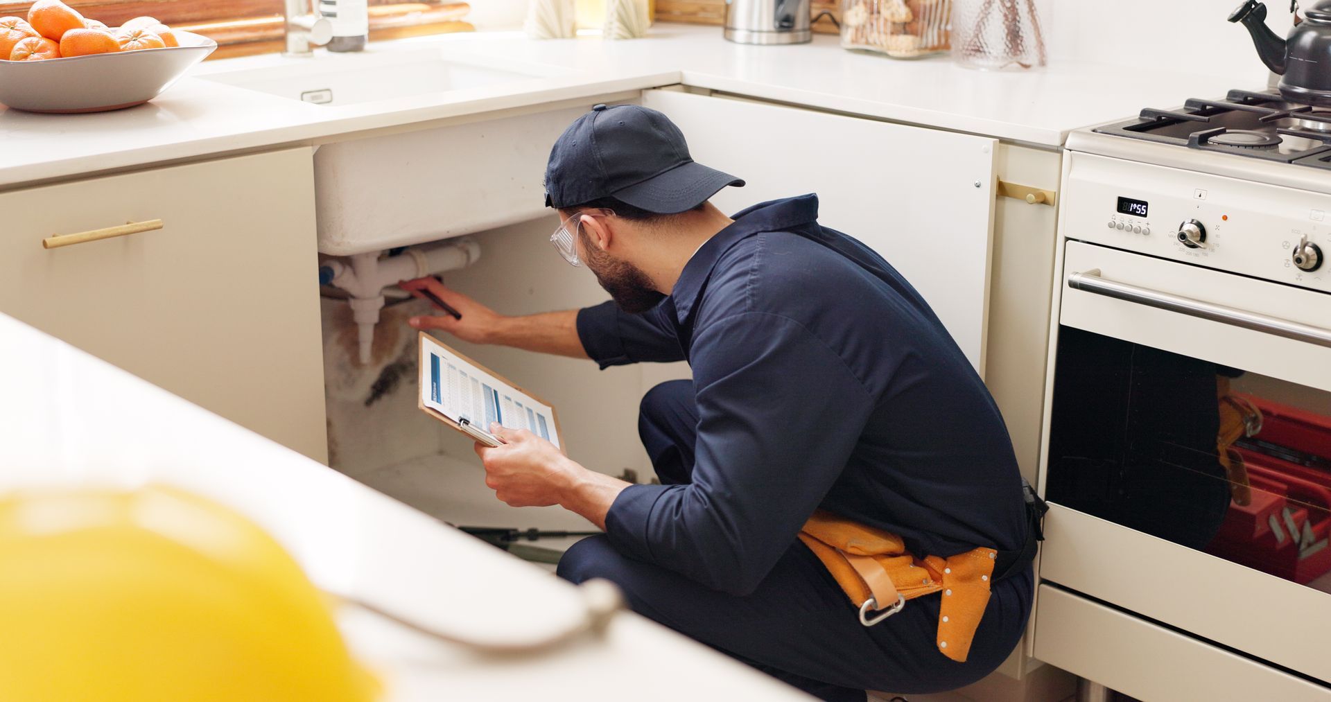 A man is kneeling down in a kitchen looking under a sink.