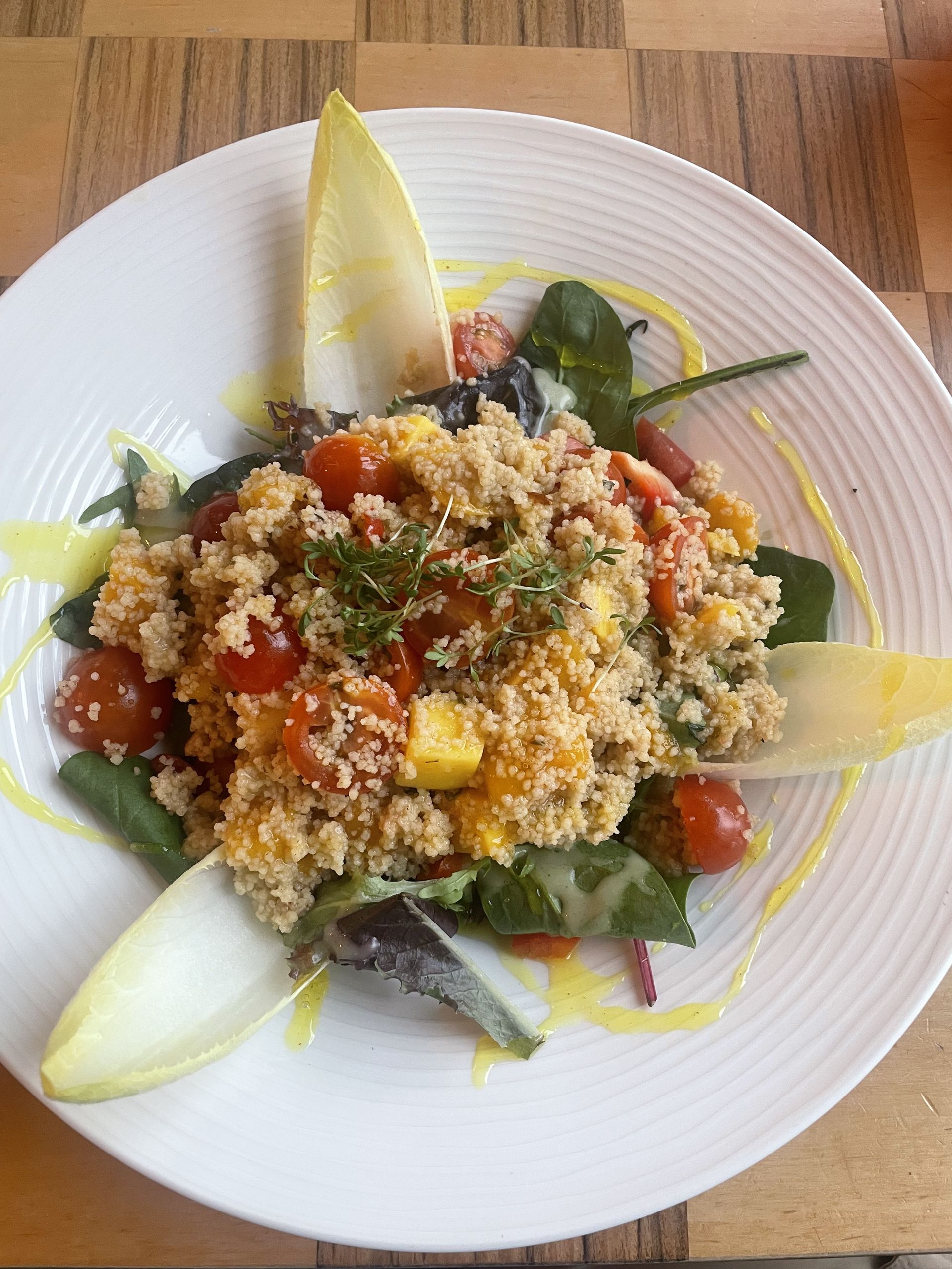 Couscous salad with tomatoes, greens, and endive.  Yellow dressing and white plate.