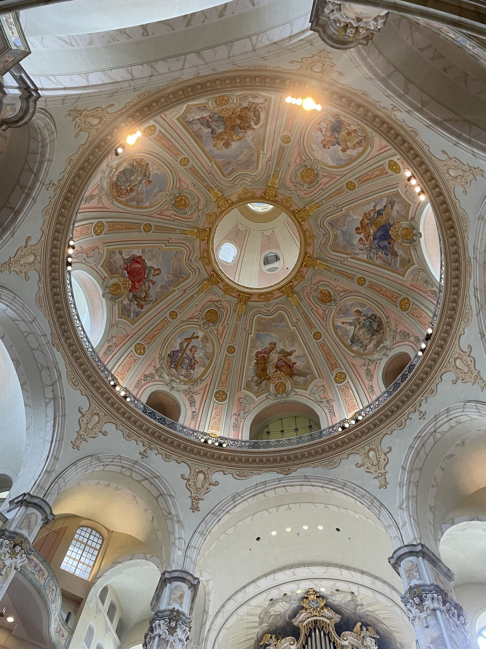Ornate, painted church dome with floral and cherubic designs, gold accents, and overhead lighting.