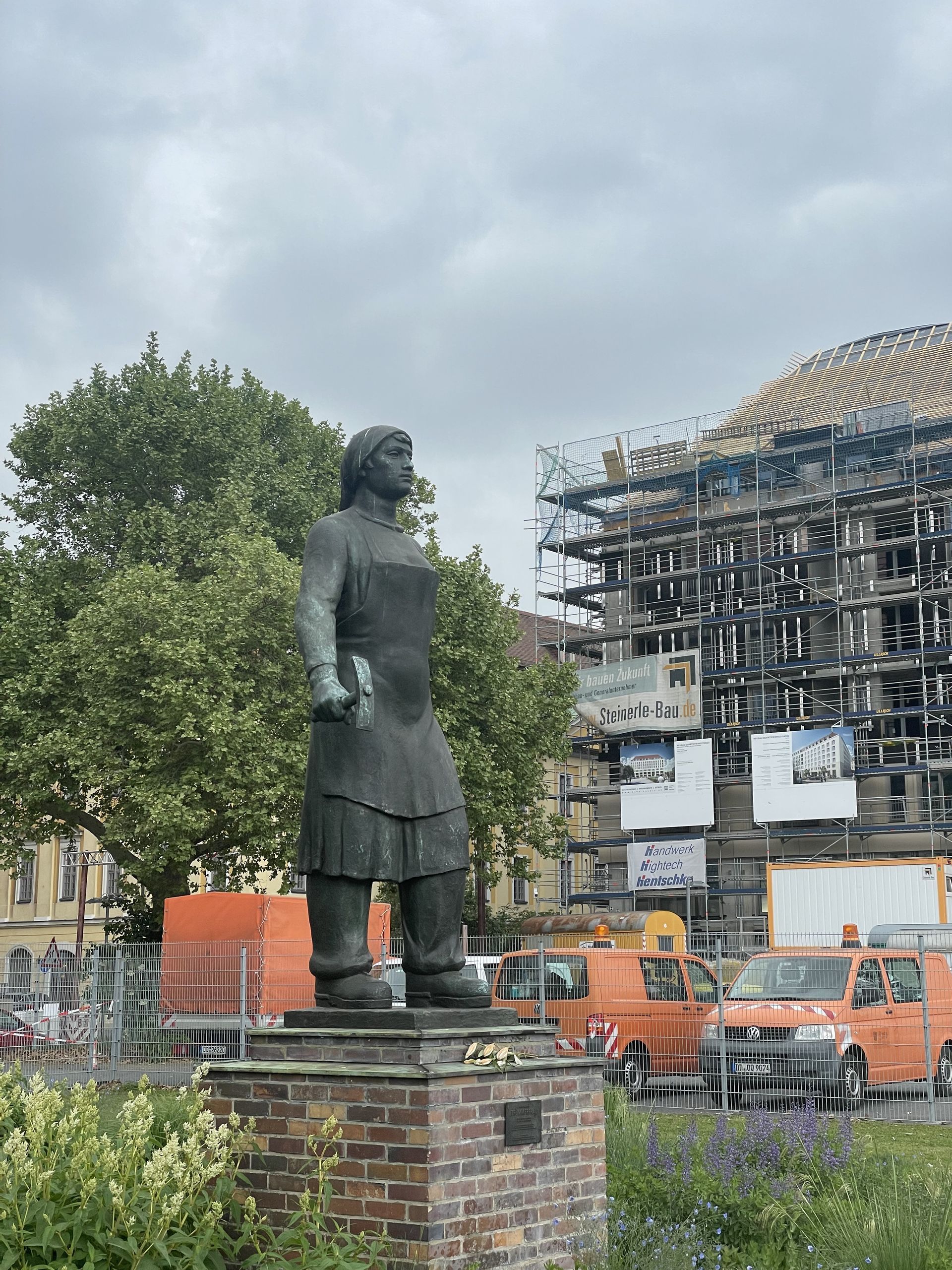 Statue of a woman with building under construction in the background, set in a city park.