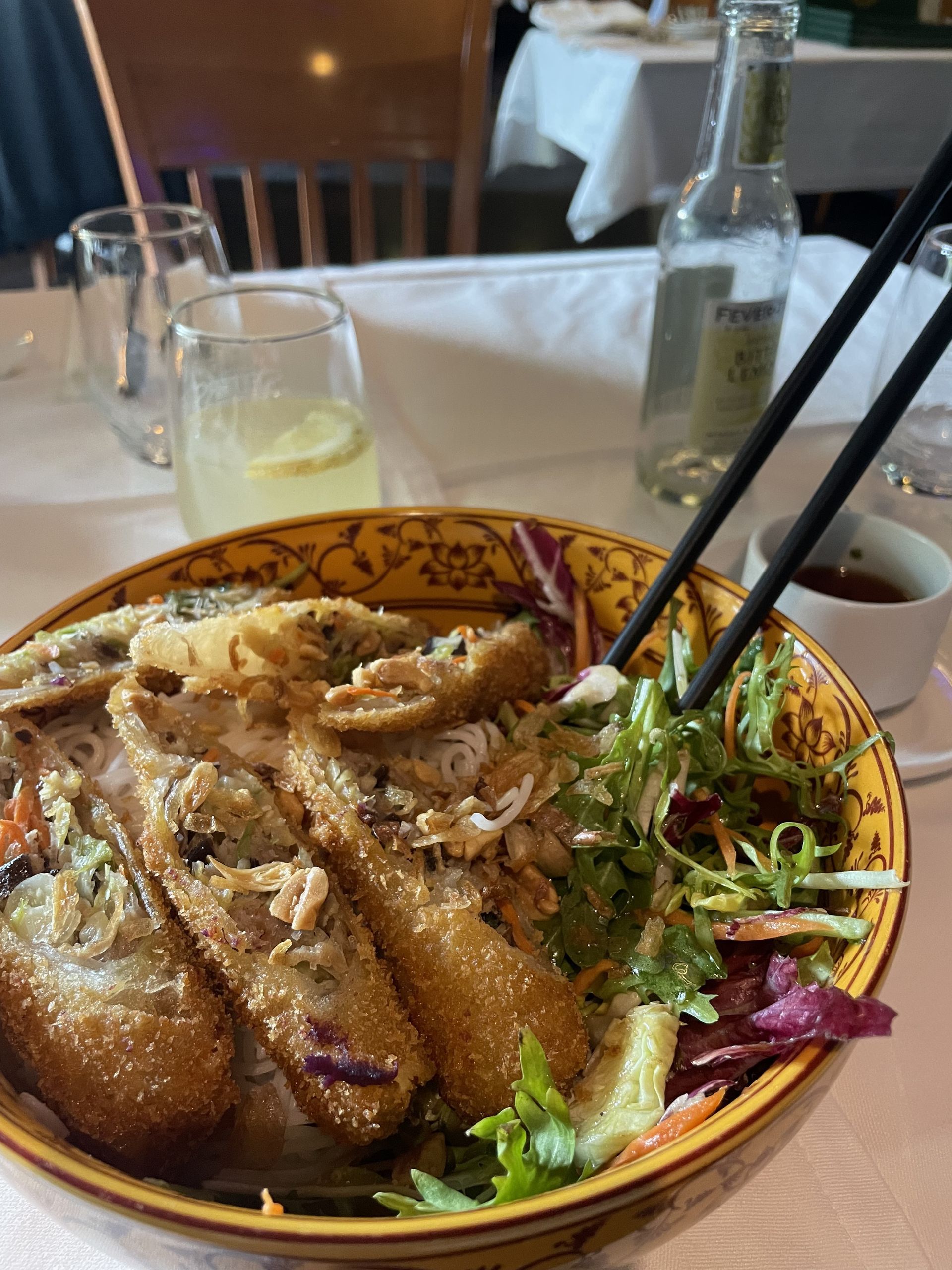 Bowl of Vietnamese food with spring rolls, noodles, and salad, chopsticks reaching in.