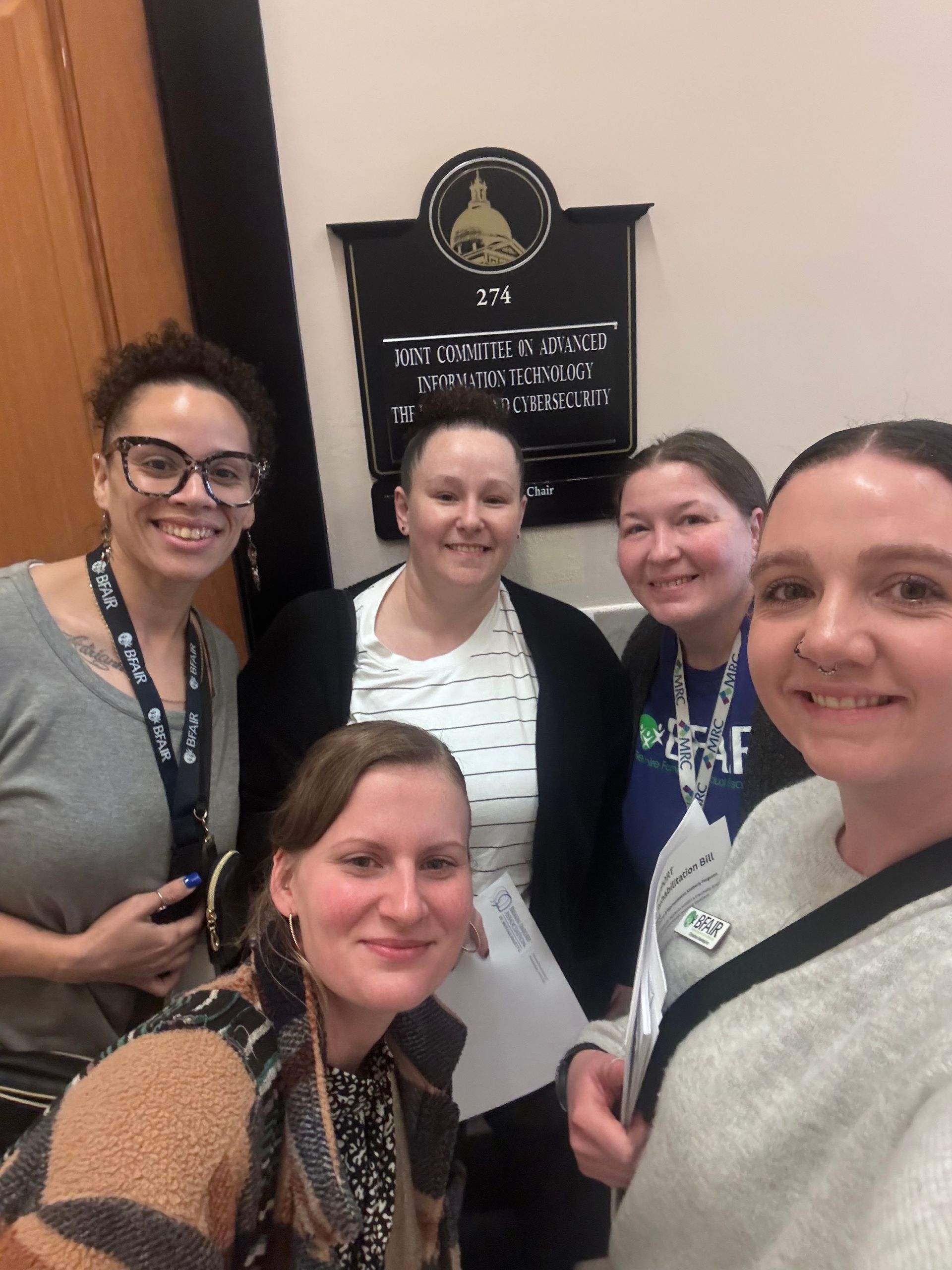 Five smiling women pose in front of a sign that reads 