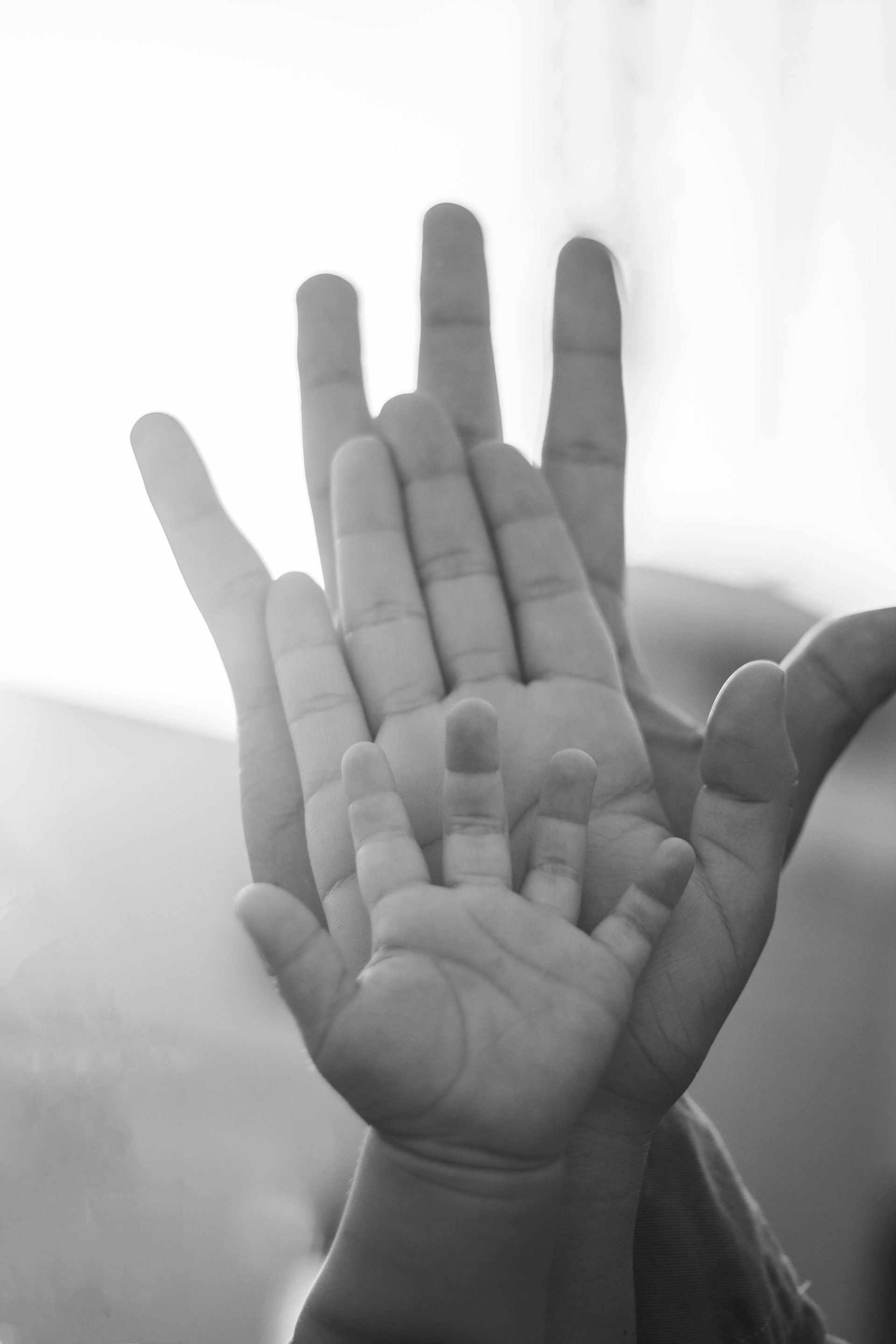 Three hands, adult, child, and baby, stacked together. Black and white.