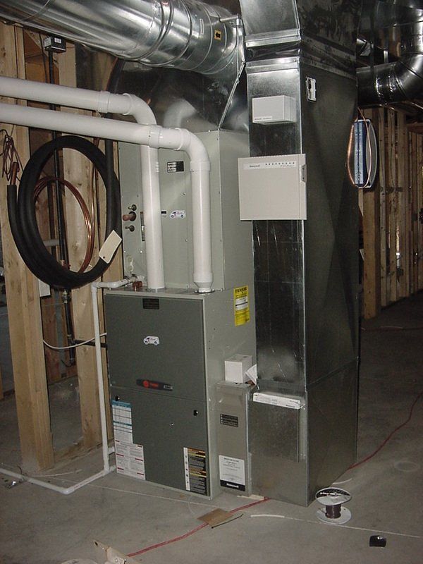 Metal HVAC units in an unfinished room with ductwork and concrete floor.