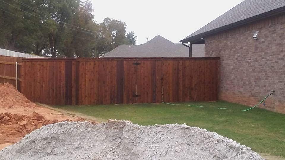 A wooden fence is in the backyard of a house next to a pile of gravel.
